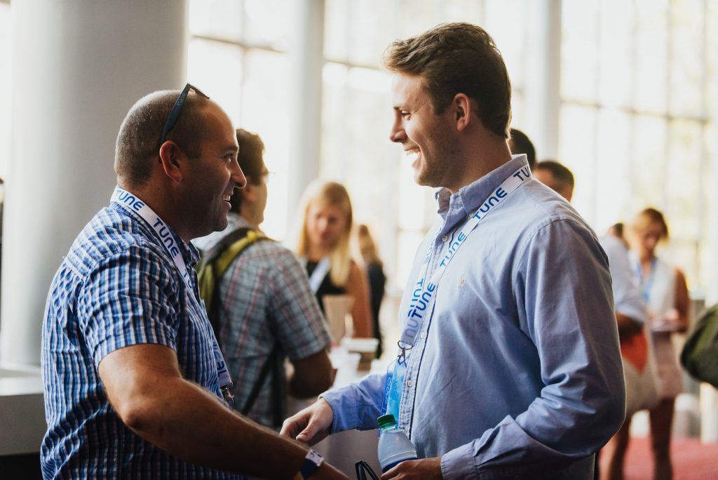 Two men shake hands as they network at Postback 2016