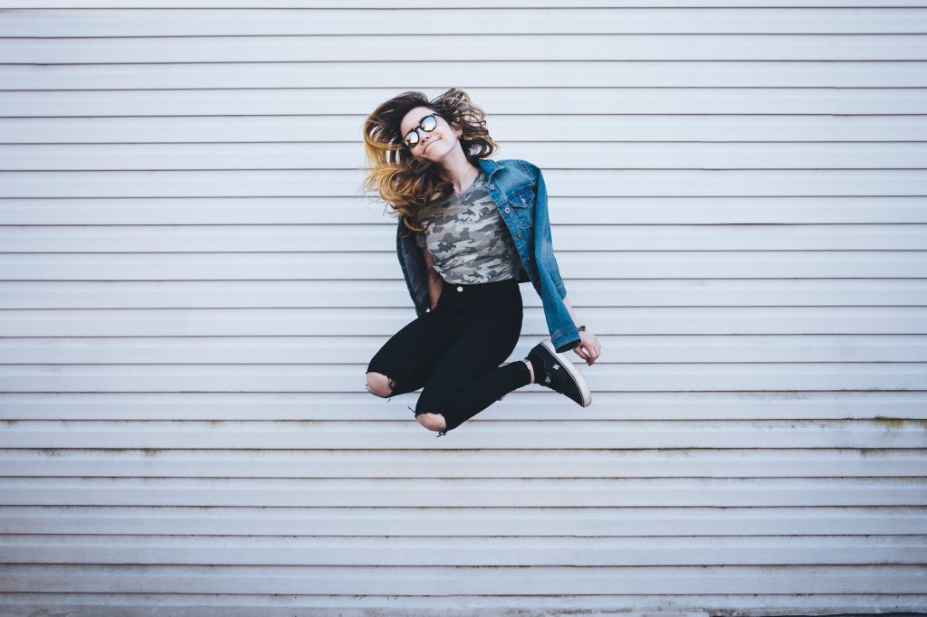 A girl jumps in front of a white wall.