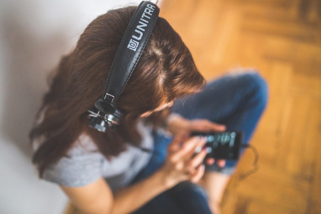 A girl listens to a podcast via headphones plugged into her phone.