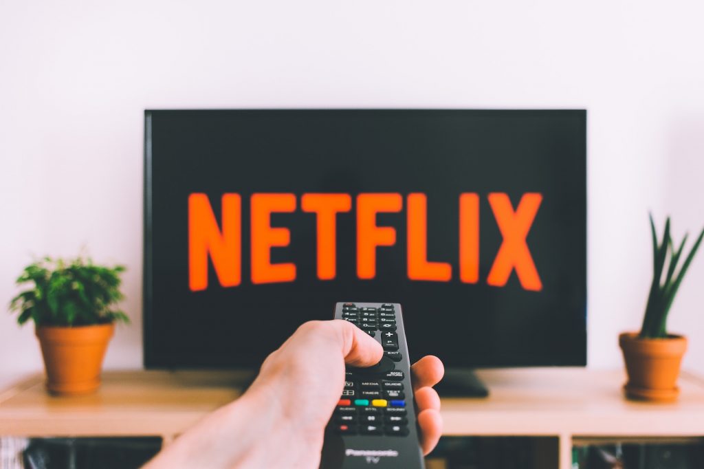 Hand holding a TV remote in front of a Netflix screen