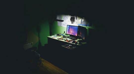A computer in a dark room overshadows the looming threat of digital advertising fraud