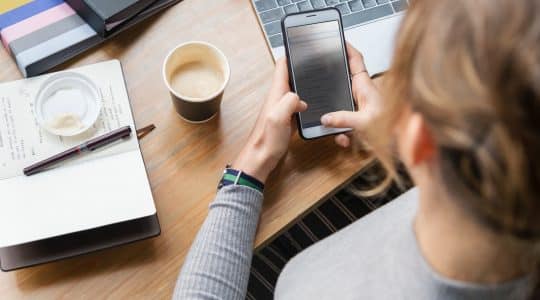 A media buyer answers emails on her mobile phone as she plans her marketing goals for the day.