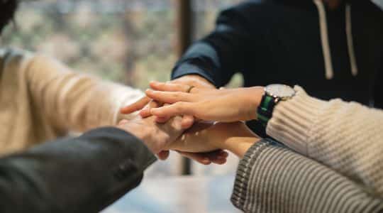 Photo of coworkers in office putting their hands in.