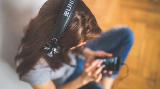 A girl listens to a podcast via headphones plugged into her phone.