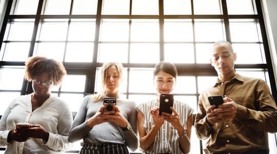 Four people browse smartphones backlit by window panes